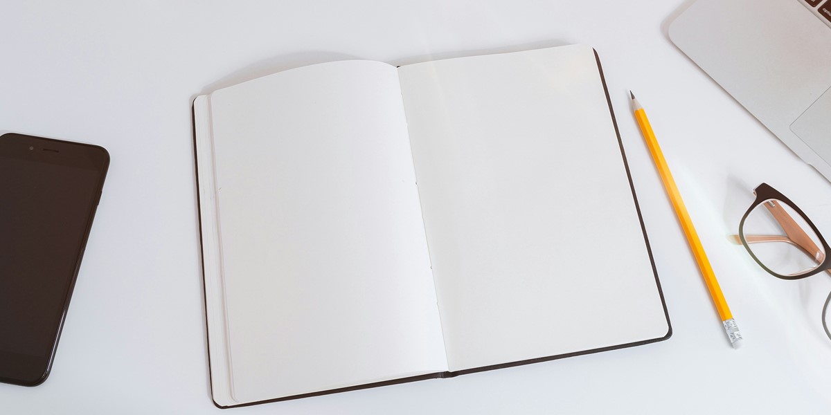 notebook on desk with pencil, phone and glasses