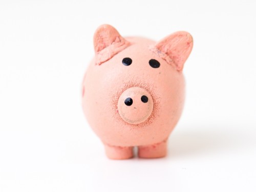 A cute, small ceramic piggy bank with a pink exterior and black eyes, facing forward on a white background.