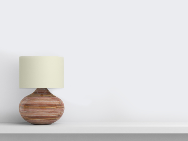 A modern lamp with a round, striped wooden base and a cylindrical white shade sits on a sleek white shelf against a light wall.
