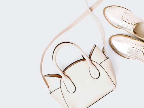 A stylish cream handbag next to elegant metallic shoes on a light grey background.