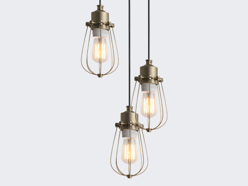 Three vintage-style pendant lights with clear glass and gold metal cages hang from black cords against a light gray background.